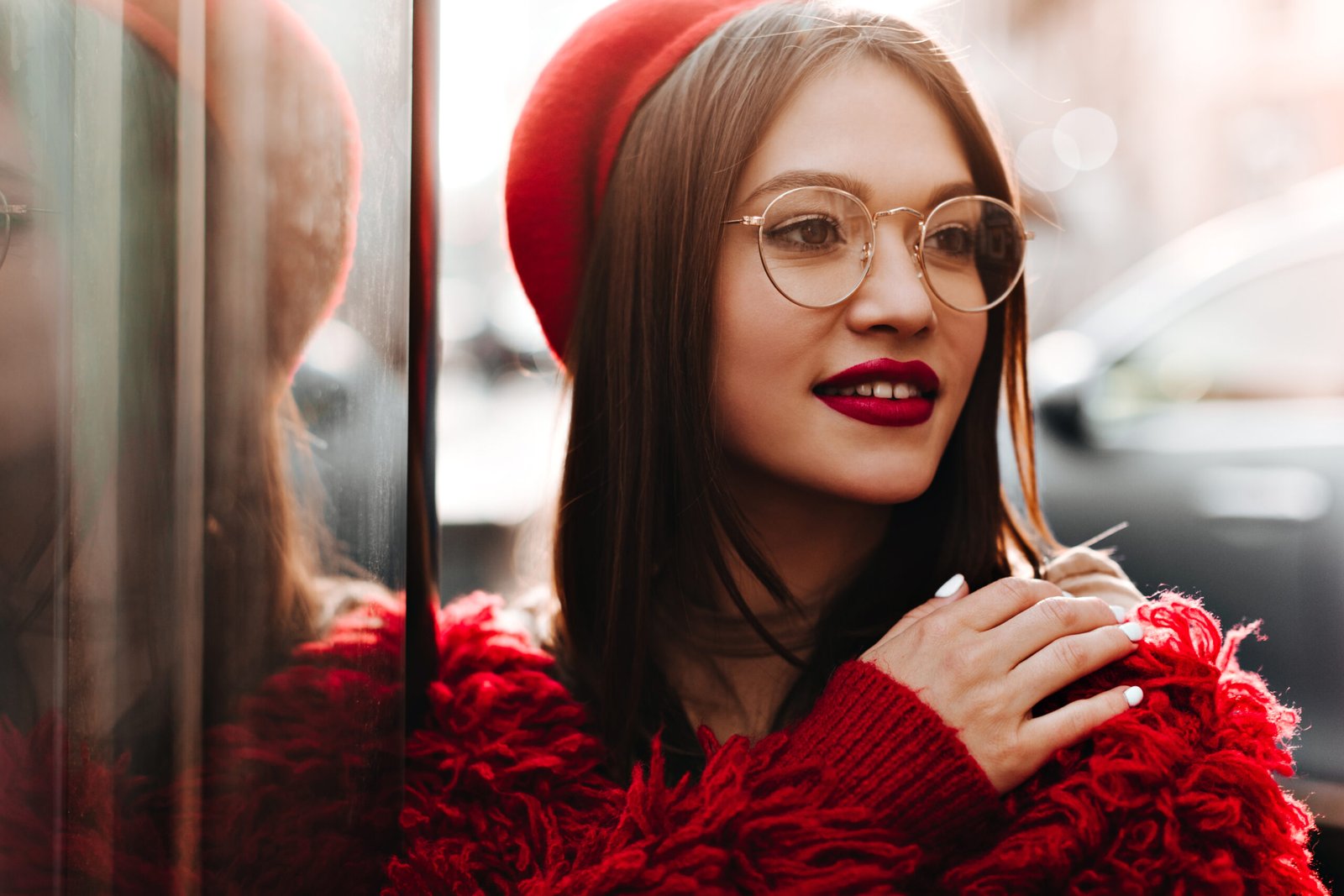 Charming girl with red lipstick in glasses walks around city. Portrait of brunette in beret in French style and knitted coat